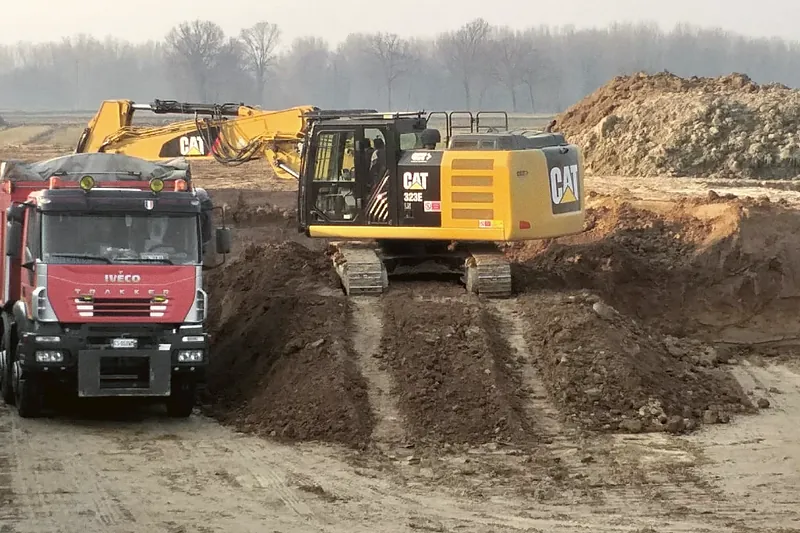 Escavatore Caterpillar al lavoro sul fronte di cava con camion in caricamento