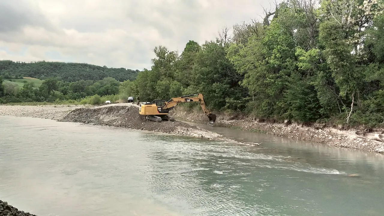 Escavatore al lavoro su opere di regimazione fluviale a scopo irriguo lungo un corso d'acqua