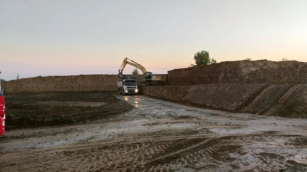 Escavatore e camion al lavoro all'alba su uno scavo di sbancamento