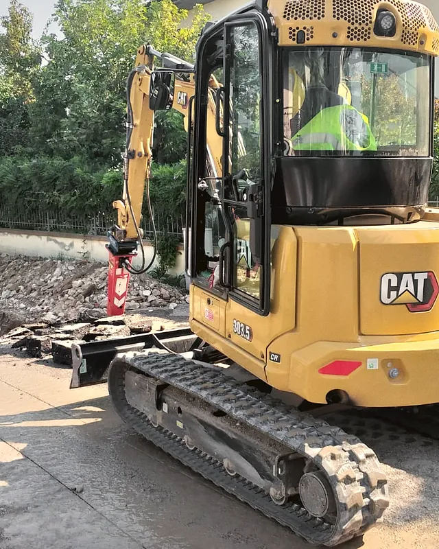 Miniescavatore Caterpillar 303.5 CR con martello demolitore Promove XP 150 durante la rimozione di una pavimentazione esistente